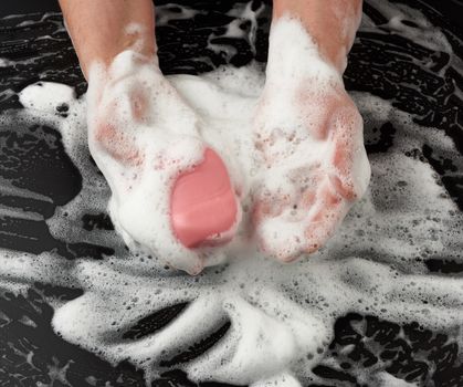 process of washing hands with pink soap, parts of the body in white foam on a black background, top view, hygiene concept