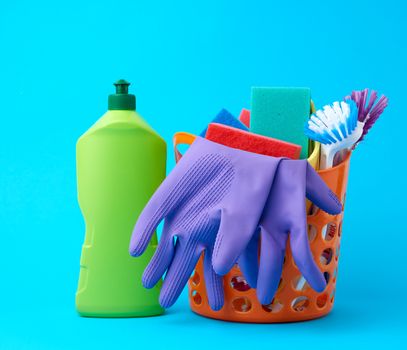 orange basket with washing sponges, rubber protective gloves, brushes and cleaning agent in a green plastic bottle on a blue background, set
