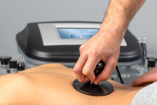 Close up detail of therapist applying electrotherapy on female spine.Professional stimulating muscle and nerves on woman.