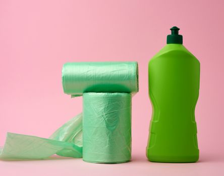 roll with transparent bags for the bin and a plastic bottle with detergent on a pink background