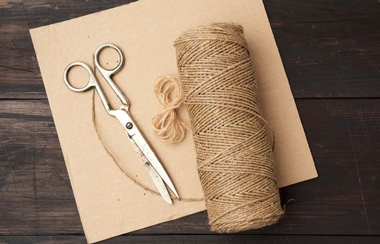 brown thread twisted into a spool and vintage metal scissors on a wooden background from boards, top view