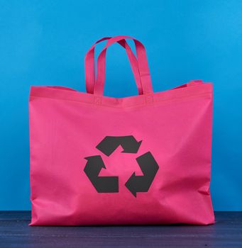 Full reusable pink viscose bag on blue wooden background, plastic waste reduction concept