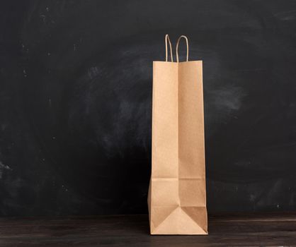 brown paper bag with handles stands on a wooden background, black background, copy space