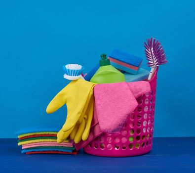 pink basket with washing sponges, rubber protective gloves, brushes and cleaning agent in a green plastic bottle on a blue background, set