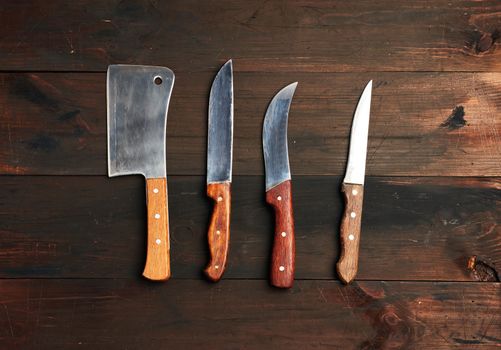 set of different kitchen knives with wooden handles on a brown background from boards, top view