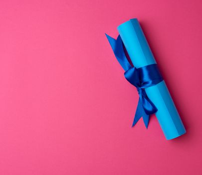 roll of blue paper tied with a silk blue ribbon, bundle on a pink background, copy space