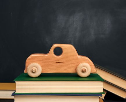 stack of books and wooden toy car on wheels, background from black chalk board, back to school