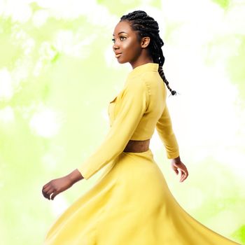 Close up studio portrait of young attractive african woman in yellow dress.Girl with braided hairstyle swaying silky dress against colorful green background.