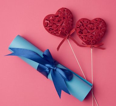 two red heart and roll of blue paper tied with a silk blue ribbon, bundle on a pink background, copy space