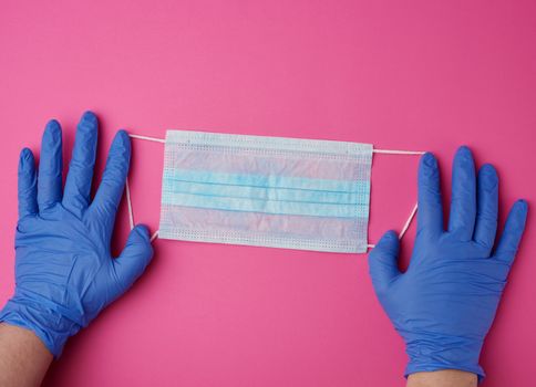 hands holds a medical mask against viruses and bacteria on a pink background, protective medical tool, top view