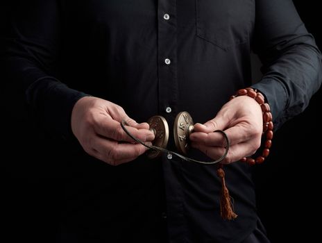 adult man in black clothes holds in his hands a pair of bronze Karatal on a leather rope, object for religious rituals, meditations and alternative medicine, low key