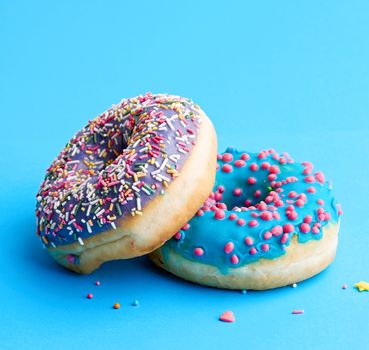 two round baked donut with colored sugar sprinkles and with blue sugar icing on a blue background