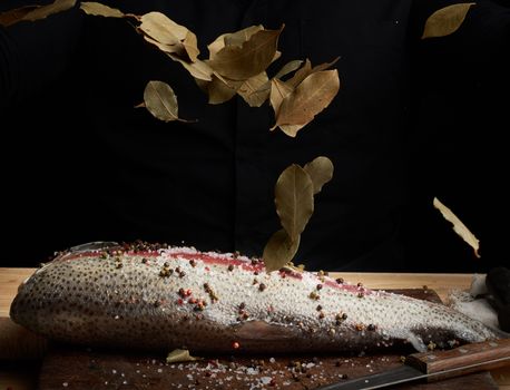 headless salmon filet on a wooden board sprinkled with leaves of dry bay leaves, process of cooking fish