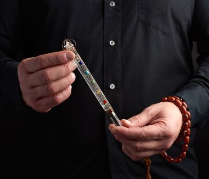 adult man in a black shirt holds a crystal chakra rod inlaid with semiprecious stones. Wand to strengthen energy and alternative medicine