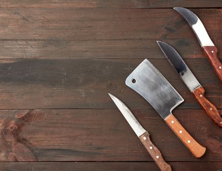 set of different kitchen knives with wooden handles on a brown background from boards, top view