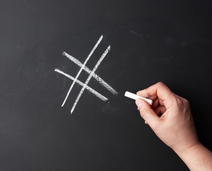 hand with chalk painted a hashtag on a black chalk board, close up