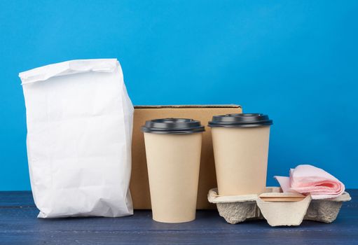 full white paper bag and brown paper disposable cups with a plastic lid stand in the tray on a blue wooden table, takeaway containers