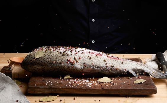 headless salmon fillet on a wooden board sprinkled with large white salt and pepper, process of cooking fish