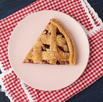 triangular slice of baked cherry pie on a pink round plate, top view