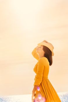 Close up portrait of young carefree woman in yellow dress at sunset. Girl with hat standing with eyes closed meditating.