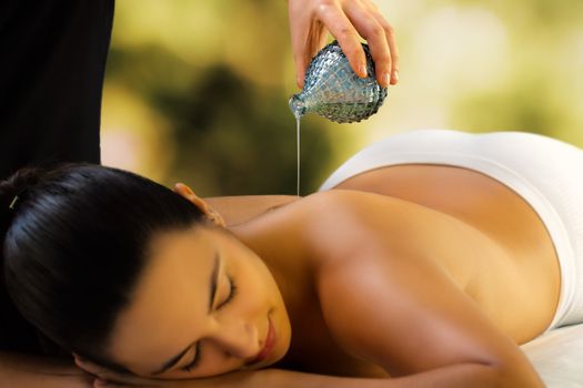 Close up of woman relaxing in low light spa.Therapist pouring massage oil on back.