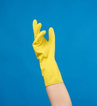yellow rubber glove for cleaning dressed on a female hand, blue background, part of the body raised up