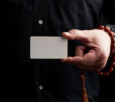 male hand holding a rectangular blank white paper business card, man wearing a black shirt, place for inscription