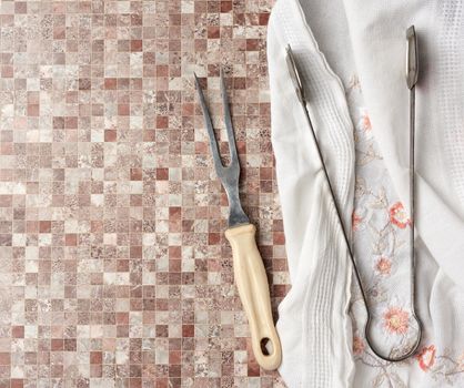 iron vintage meat fork and tongs on a white kitchen towel, top view