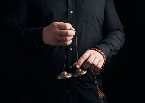 adult man in black clothes holds in his hands a pair of bronze Karatal on a leather rope, object for religious rituals, meditations and alternative medicine, low key