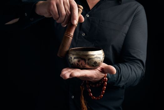 adult man in a black shirt rotates a wooden stick around a copper Tibetan bowl of water. ritual of meditation, prayers and immersion in a trance. Alternative treatment