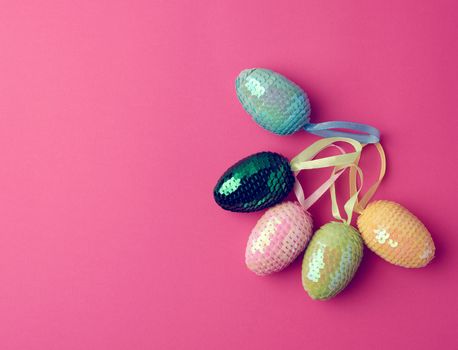 multicolored decorative Easter eggs decorated with sequins on a pink background, festive background, top view, copy space
