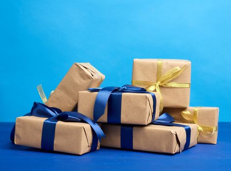 bunch of gifts in boxes wrapped in brown kraft paper and tied with silk ribbons on a blue background, festive backdrop for birthday, Christmas