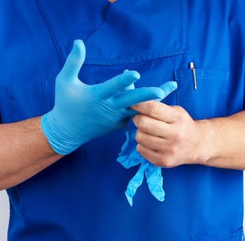 adult male doctor in blue uniform puts on his hands blue sterile latex gloves before surgery, white background