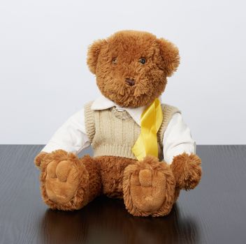 brown teddy bear sits and a yellow silk ribbon on a black wooden background, concept of the fight against childhood cancer, problem of suicides and their prevention