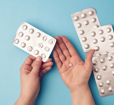 two hands hold a package of round tablets in blister packs, blue background, top view