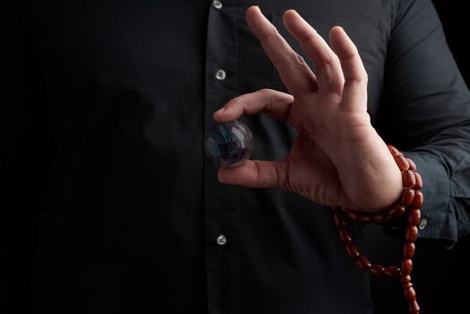 adult man in black clothes holds in his hands a glass magic ball, object for religious rituals, meditations and alternative medicine