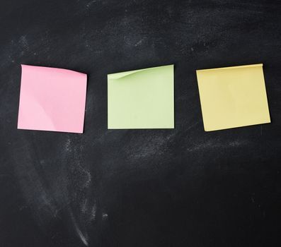 three blank paper multi-colored square stickers are stuck on a black chalk board