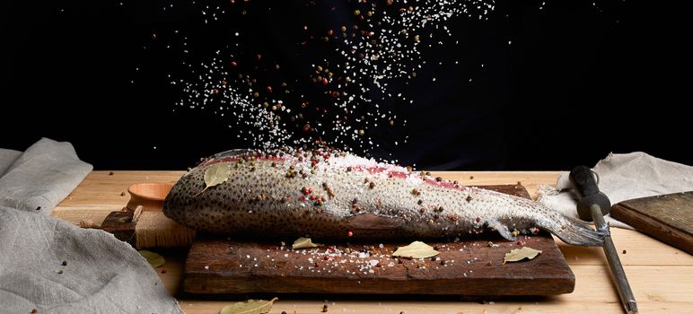 headless salmon fillet on a wooden board sprinkled with large white salt and pepper, process of cooking fish, low key