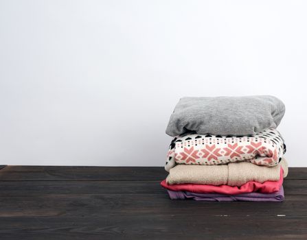 stack of various folded clothes on a wooden table, white background, place for an inscription