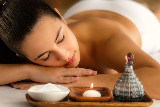 Low candle light portrait of woman relaxing in spa next to massage oil and beauty product.