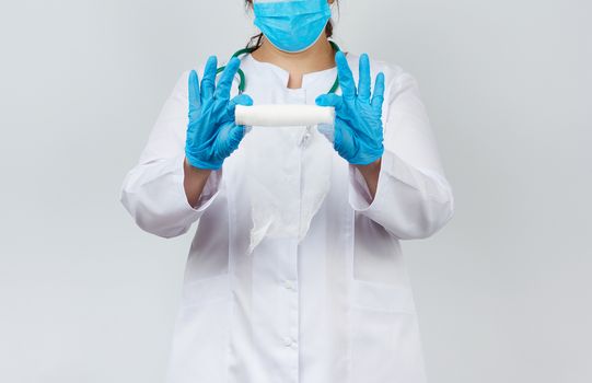 medic woman in white coat and mask holds a twisted gauze bandage for dressing wounds, white background