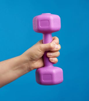 female hand holds a plastic pink dumbbell on a blue background, sport concept