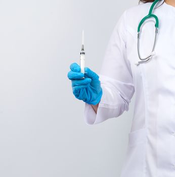 medic woman in white coat and blue latex gloves holding a syringe, white studio background, concept of timely vaccination against viruses