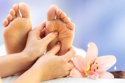 Macro close up of hands massaging female foot. Feet next to flower and candle against colourful background.