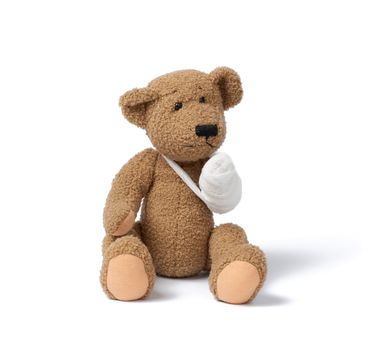 funny vintage brown curly teddy bear with rewound paw with white gauze bandage isolated on white background, concept of injuries in children or animals