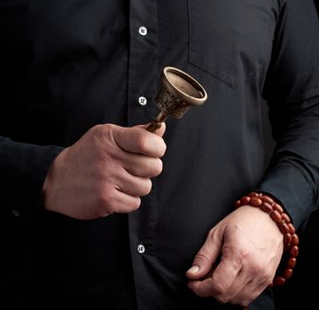 adult man in a black shirt holds a copper Tibetan ritual bell, low key. bell represents the feminine principle of excellence in wisdom.