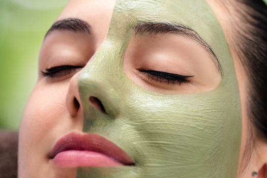 Macro close up portrait of woman having facial cosmetic green algae treatment in spa.