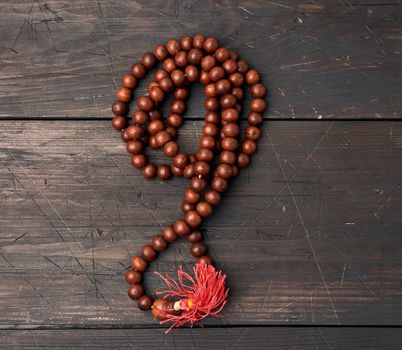 wooden prayer rosary on a brown wooden table, top view, close up