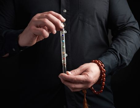 adult man in a black shirt holds a crystal chakra rod inlaid with semiprecious stones. Wand to strengthen energy and alternative medicine