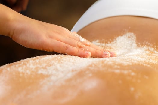 Close up detail of hand doing therapeutic salt massage on female spine.